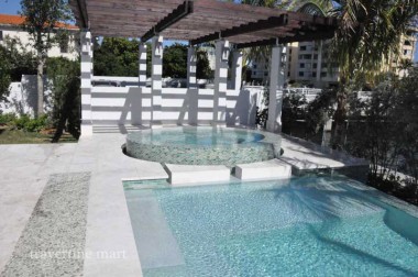 Pale square paving surrounds a pool and circular raised spa beneath a timber pergola and white garden walls.