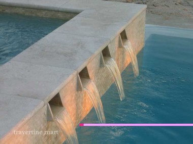 A close view shows pale stone coping above a row of rectangular spillway openings pouring into blue pool water.