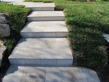 Wide light stone steps ascend between low hedges, lawn and landscaping rocks.