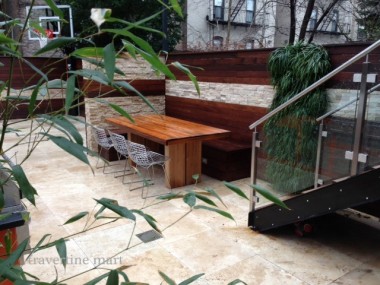 Pale square paving sits beneath wood stairs, glass railings and built-in benches in a compact planted courtyard.