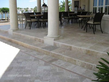 Light rectangular pavers cover a columned dining terrace and broad steps leading to the lower paved area.