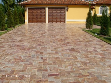 Cream, tan and russet rectangular pavers form a driveway leading to wooden garage doors at a yellow house.