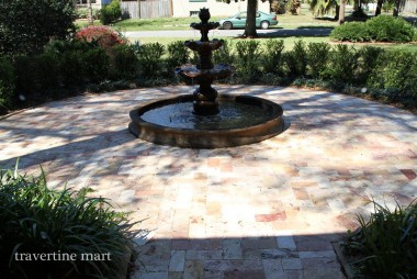 Small rectangular pavers in cream, tan and rust tones form a shaded fountain court bordered by hedges and planting.