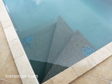 A close view shows narrow stone coping beside blue water and dark submerged steps with small blue mosaic accents.