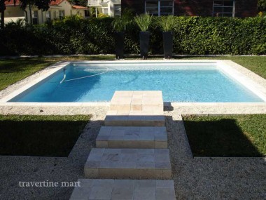 A narrow strip of square pale pavers crosses a gravel bed and projects into a small square blue pool.