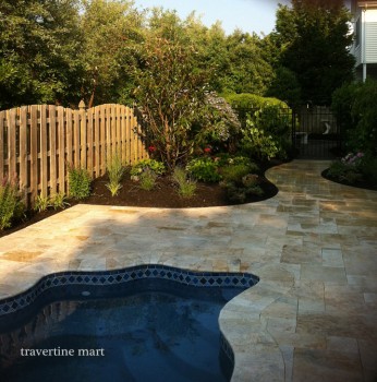 Cream and tan mixed-size paving curves beside a pool and planted garden beds along a timber fence.