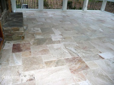 Light cream and rust-toned tiles meet the stone base of a porch fireplace and continue toward a black railing.