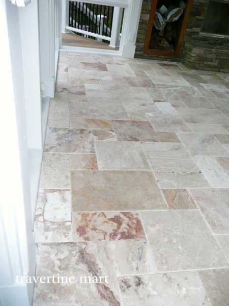 Light cream and rust-toned mixed-size tiles form a narrow porch walkway beside white walls and black railings.