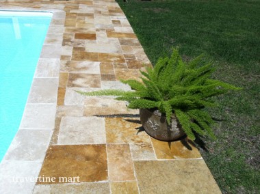 Gold and cream mixed-size paving borders blue pool water and grass, with a potted fern on the deck.