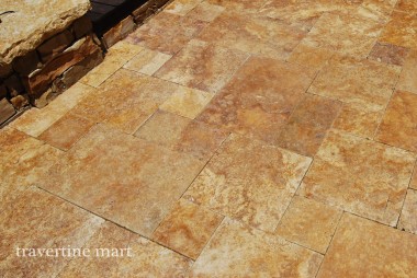 A close view of golden mixed-size paving shows mottled stone surfaces beside a rough stone wall.