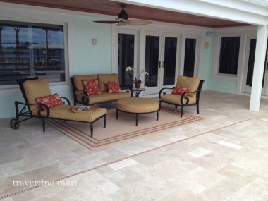 A pale mixed-size paved patio holds cushioned seating and a low table outside sliding doors beneath a ceiling fan.