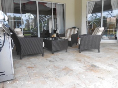 Mixed-tone stone paving continues beneath a covered lounge area with dark woven chairs and a low table.