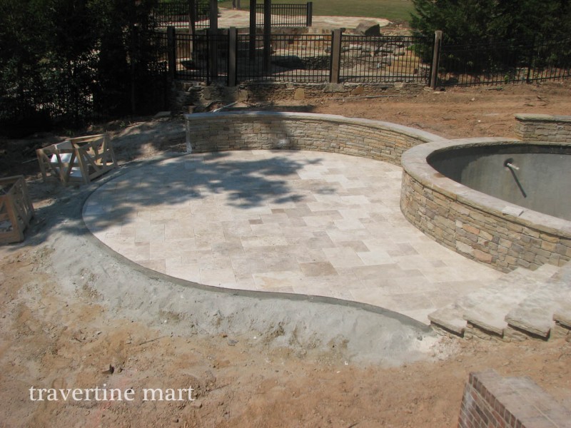 A rounded stone-paved seating area meets a curved stacked-stone wall and raised circular spa during construction.