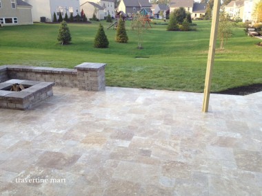 Light mixed-size pavers cover a pergola patio beside a stone seating wall, overlooking lawn and neighboring houses.