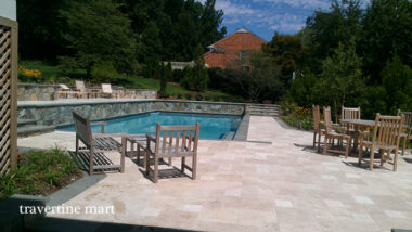 Light mixed-size paving links a rectangular pool, wooden outdoor seating and a planted retaining wall.