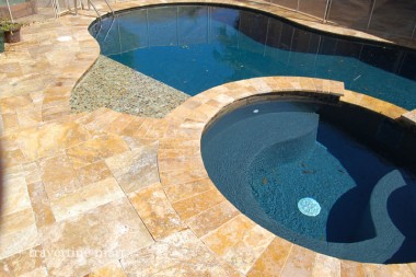 Golden mixed-size paving wraps a curved mosaic-lined spa that opens into a blue pool.
