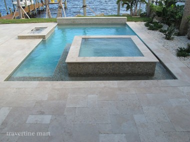 Pale mixed-size paving surrounds a rectangular pool and raised square spa with steps and open water beyond.
