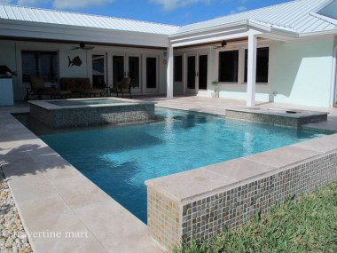 Light stone coping edges a rectangular pool and raised spa beside a covered house patio with white posts.