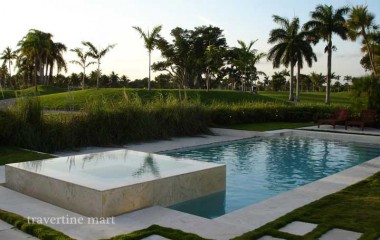 Pale stone edging and lawn-set stepping slabs surround a rectangular pool with a raised square basin and tall grasses.