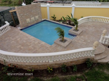 Brown rectangular pavers cover a pool courtyard bordered by curved white balustrades, palms and yellow walls.