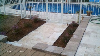 A narrow pale paved path crosses a planting bed between a timber deck and a pool terrace with light railings.
