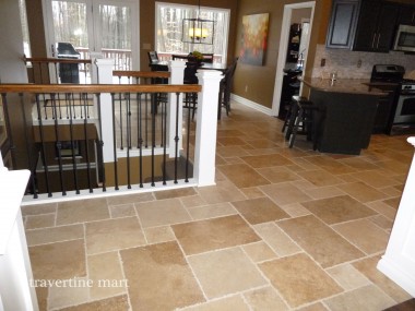 Warm brown mixed-size tiles link a kitchen, dining area and stair railing with white posts and dark balusters.