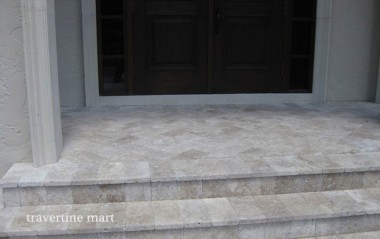 Small pale rectangular pavers cover an entry landing and broad steps beneath a pair of dark doors.