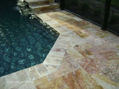 A close view shows warm mixed-size pavers following an angular pool edge beneath a screened enclosure.