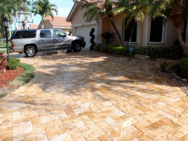 Small golden pavers cover a planted driveway beside a house, with a parked pickup truck at the edge.