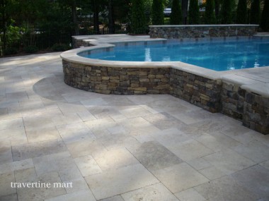 Pale mixed-size paving curves around a raised circular spa faced with stacked stone and capped with light stone.