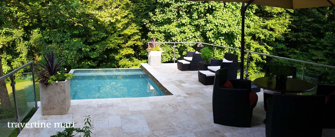 Mixed-size pale paving around a garden pool with shaded seating and dense greenery.