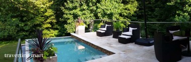 A garden pool sits below a paved seating terrace with black lounge chairs and glass railings among trees.