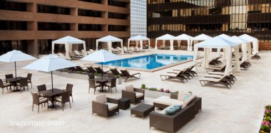 Light rectangular paving surrounds a courtyard pool with white umbrellas, cabanas, chaise lounges and clustered seating.