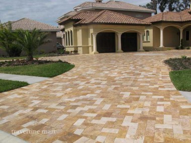 Gold and pale cream rectangular pavers create a two-tone driveway leading to a house with an arched covered porch.