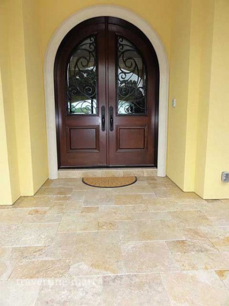Cream and tan mixed-size pavers form an entry landing beneath an arched timber double door with decorative glass.