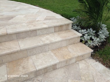 Broad pale stone steps connect garden paving beside lawn and a bed of white and green foliage.